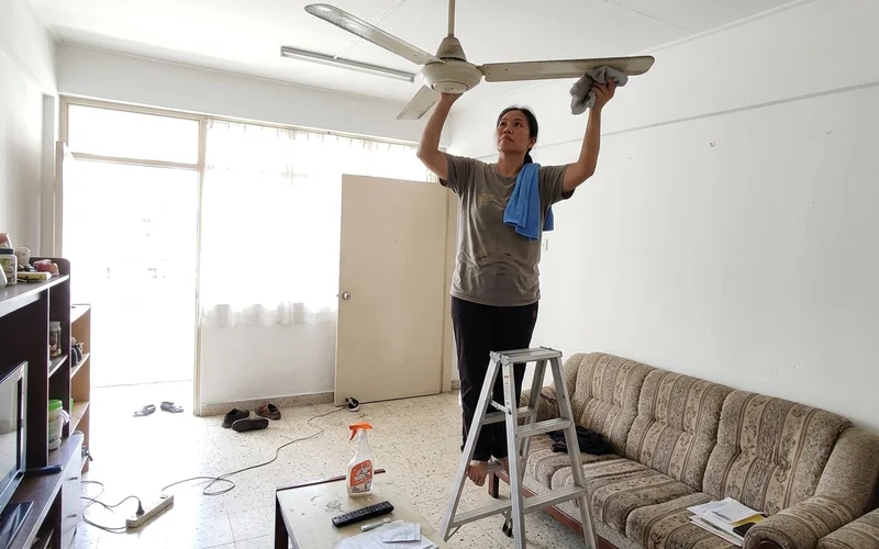 Cleaner wiping ceiling fan blades on a step stool